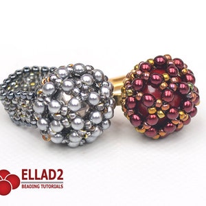 May include: Two beaded rings, one silver and one red with gold accents. The rings are made with small beads and have a round shape.