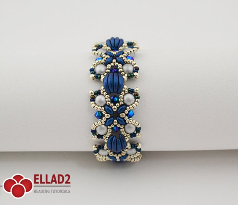Op de afbeelding: Een blauwe en zilveren kralen armband met een bloemenmotief. De armband is gemaakt met kleine, ronde kralen en heeft een delicaat, ingewikkeld patroon.