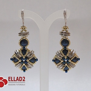 May include: A pair of handcrafted dangle earrings. The earrings feature a silver-tone metal and gold-tone beads, with dark blue accents. The design includes a square shape with a central dark blue bead and a decorative top.