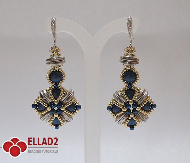 May include: A pair of handcrafted dangle earrings. The earrings feature a silver-tone metal and gold-tone beads, with dark blue accents. The design includes a square shape with a central dark blue bead and a decorative top.