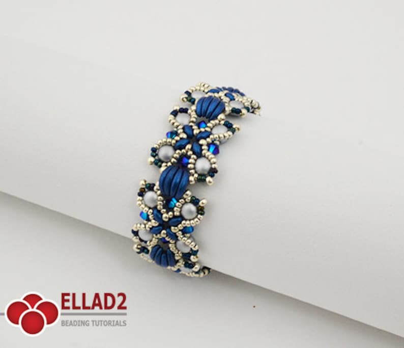 Op de afbeelding: Een blauwe en zilveren kralen armband met een bloemenpatroon. De armband is gemaakt met kleine kraaltjes en grotere ronde kralen.