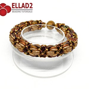 Peut inclure: Un bracelet en perles dor&eacute;es, brunes et violettes avec un fermoir magn&eacute;tique. Le bracelet est fait de petites perles de rocaille et est pr&eacute;sent&eacute; sur un support transparent.