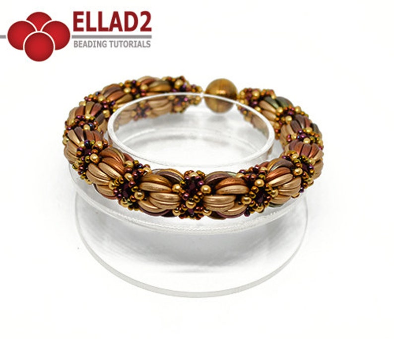 Peut inclure: Un bracelet en perles dor&eacute;es, brunes et violettes avec un fermoir magn&eacute;tique. Le bracelet est fait de petites perles de rocaille et est pr&eacute;sent&eacute; sur un support transparent.