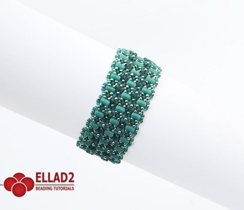 Op de afbeelding: Een turquoise en zilveren kralenarmband met een geometrisch patroon. De armband is gemaakt met kleine, vierkante kralen en is ongeveer 5 cm breed.