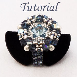 May include: A silver and blue beaded ring with a large blue crystal in the center. The ring is on a black velvet ring display.