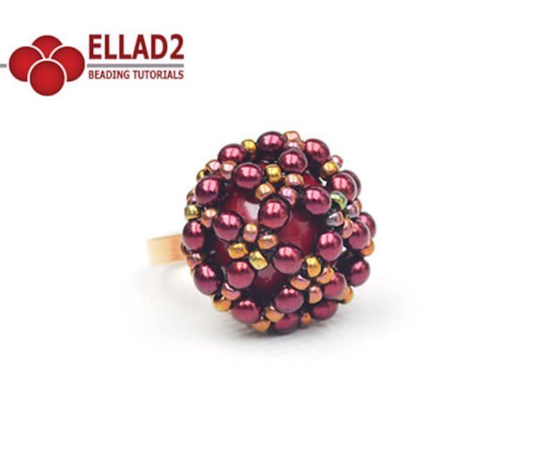 May include: A burgundy and gold beaded ring with a large, round, burgundy bead in the center. The ring is made with small, round beads that are arranged in a geometric pattern.