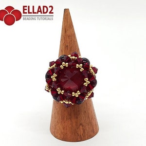 Może przedstawiać: Pierścionek z czerwonych i złotych koralik&oacute;w z dużym czerwonym kamieniem szlachetnym w środku. Pierścionek jest prezentowany na drewnianym stojaku na pierścionki.  ELLAD2 Beading Tutorials.