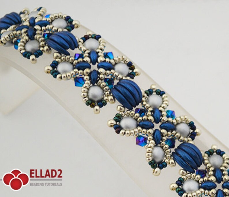 Op de afbeelding: Een kralenarmband met een blauwe, zilveren en gouden kleurstelling. De armband heeft een herhalend patroon van bloemvormige vormen.