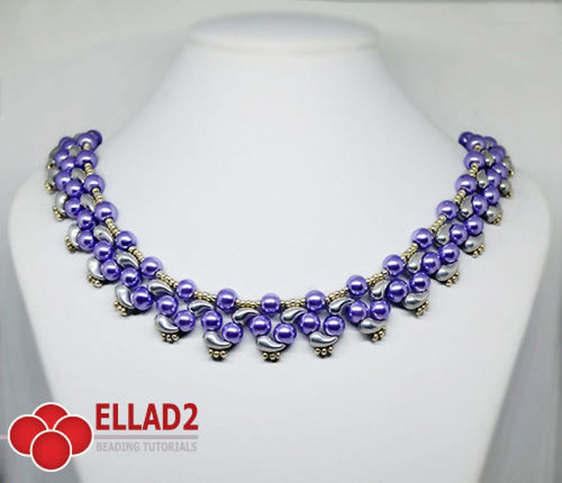 May include: A beaded necklace with a curved design. The necklace features lavender and silver beads, with gold-colored accents. The necklace is displayed on a white mannequin. The text "ELLAD2 BEADING TUTORIALS" is visible in the lower left corner.