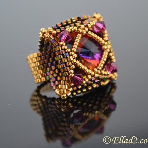 May include: A square-shaped ring with a large, faceted, iridescent purple and orange gemstone surrounded by smaller, purple gemstones. The ring is made of gold-colored beads and has a woven design.