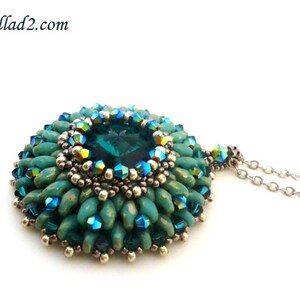 Op de afbeelding: Een ketting met een hanger van turquoise en groene kralen, met in het midden een grote, gefacetteerde, donkergroene edelsteen. De hanger is omringd door kleinere, iriserende kralen.