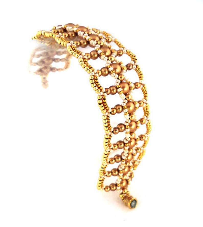 K&ouml;nnte beinhalten: Ein goldfarbenes und cremefarbenes Armband mit geometrischem Muster. Das Armband besteht aus kleinen runden Perlen und hat einen Verschluss.