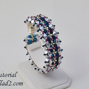 Könnte beinhalten: Ein silbernes, blaues und pinkfarbenes Armband mit einem Verschluss. Das Armband befindet sich auf einem weißen Präsentationsständer. Tutorial ellad2.com