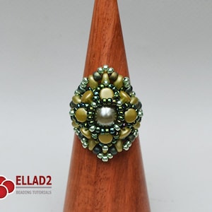 May include: A green and gold beaded ring with a pearl in the centre, displayed on a wooden ring stand.