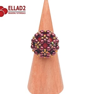 May include: A red, gold, and green beaded ring on a wooden ring holder. The ring is made of small beads and has a geometric design.