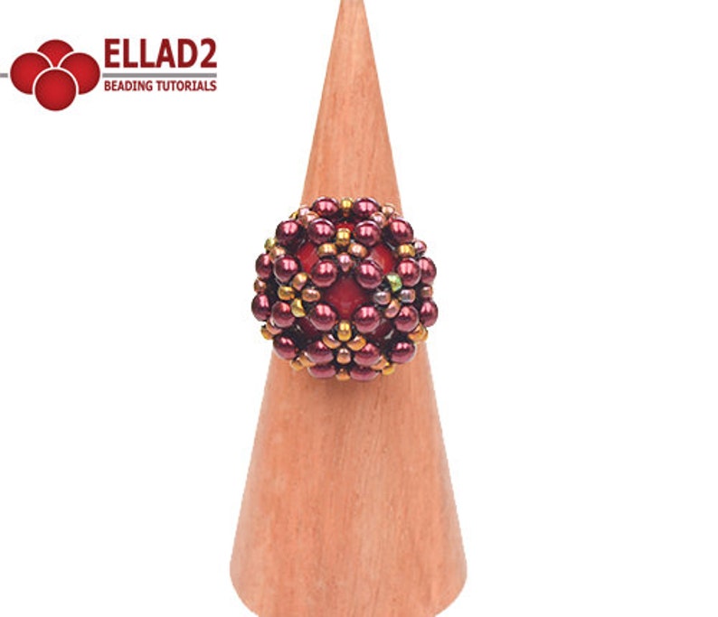May include: A red, gold, and green beaded ring on a wooden ring holder. The ring is made of small beads and has a geometric design.