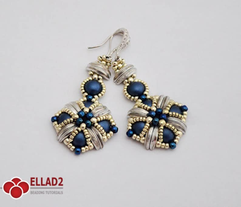 May include: A pair of handmade earrings with a silver and gold design. The earrings feature a square shape with navy blue beads and silver accents. The earrings have a decorative hook and are designed for pierced ears.