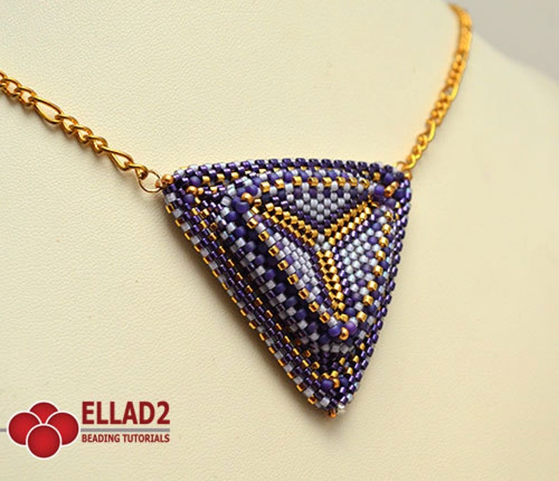 May include: A purple and gold beaded triangle pendant necklace with a gold chain. The pendant is made of small beads in a geometric pattern. The necklace is a statement piece and would be a great addition to any jewelry collection.