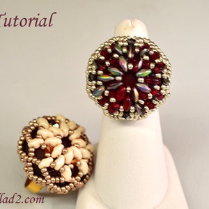 May include: Two beaded rings, one with a red and silver design and the other with a white and gold design. The rings are on display on a white stand. The word "Tutorial" is written in maroon at the top of the image.