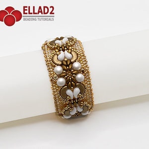 Puede incluir: Un brazalete de cuentas doradas y blancas con un diseño floral. El brazalete está hecho con cuentas de semillas pequeñas y cuentas blancas más grandes.