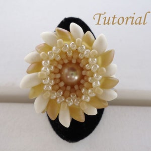 Op de afbeelding: Een handgemaakte bloemenring met een centrale parel omringd door crème- en bruinachtige bloemblaadjes. De ring staat op een zwart fluwelen display. Het woord "Tutorial" is in cursief geschreven.