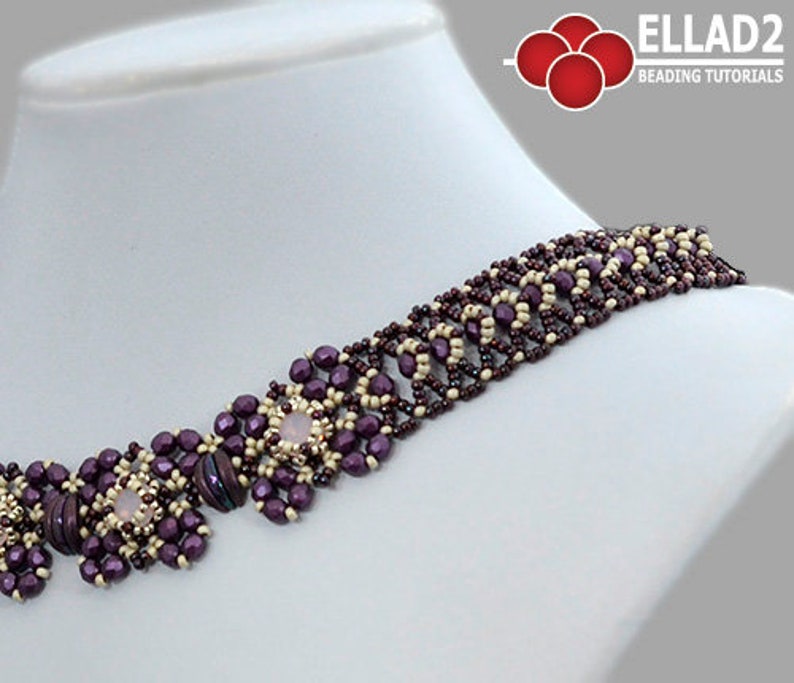 May include: A close-up of a beaded necklace with a geometric pattern. The necklace is made with purple and cream beads and features a central design with larger, pink beads. The necklace is on a white mannequin.