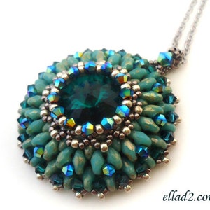 Op de afbeelding: Een ketting met een hanger van teal groene kralen met een grote, gefacetteerde, smaragdgroene edelsteen in het midden. De hanger is omgeven door kleinere, iriserende kralen.