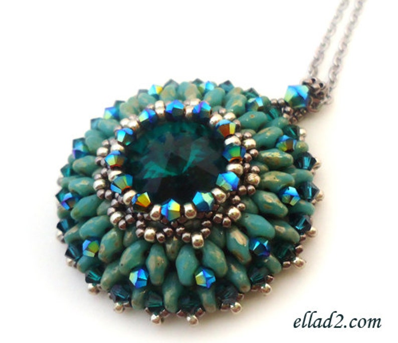 Op de afbeelding: Een ketting met een hanger van teal groene kralen met een grote, gefacetteerde, smaragdgroene edelsteen in het midden. De hanger is omgeven door kleinere, iriserende kralen.