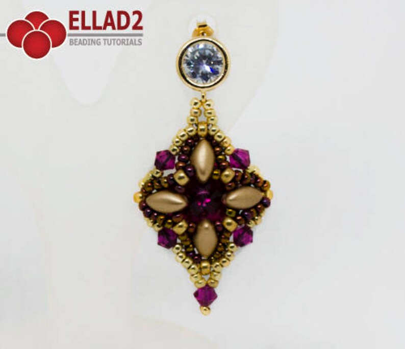 Peut inclure: Boucles d'oreilles pendantes en perles dor&eacute;es et violettes avec un strass transparent au sommet. Les boucles d'oreilles ont la forme d'un diamant avec un motif floral au centre.