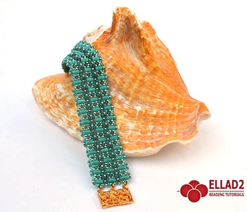 Op de afbeelding: Een tealblauwe kralenarmband met een gouden metalen sluiting. De armband wordt getoond op een schelp.