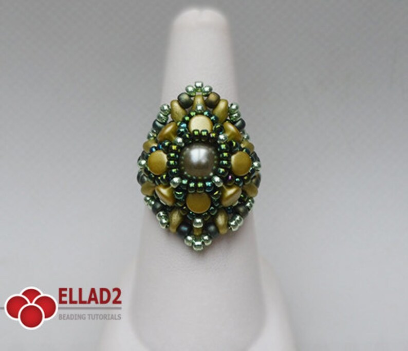 May include: A green and gold beaded ring with a pearl in the center. The ring is on a white display stand.