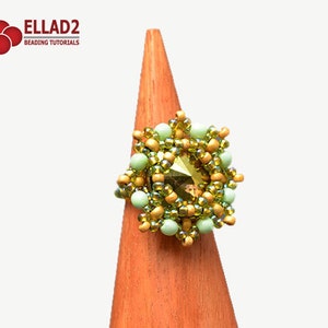 K&ouml;nnte beinhalten: Ein gr&uuml;ner und goldener Perlenring mit einem klaren Kristall in der Mitte. Der Ring befindet sich auf einem h&ouml;lzernen Ringst&auml;nder.