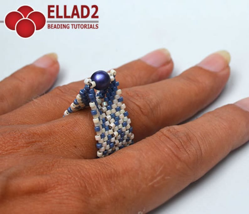 Peut inclure: Une bague perl&eacute;e faite &agrave; la main, bleue et blanche, orn&eacute;e d'une perle centrale bleu fonc&eacute;. La bague est compos&eacute;e de petites perles carr&eacute;es dispos&eacute;es en motif tiss&eacute;. Le texte "ELLAD2 BEADING TUTORIALS" est &eacute;galement visible.
