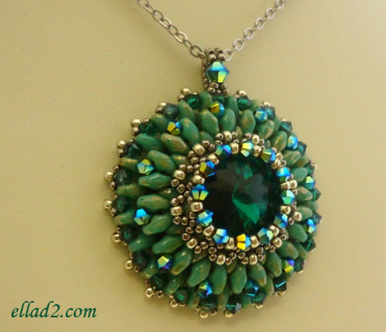 Op de afbeelding: Een groene en zilveren kralenketting met een grote smaragdgroene edelsteen in het midden. De hanger is omringd door kleinere groene en zilveren kralen.