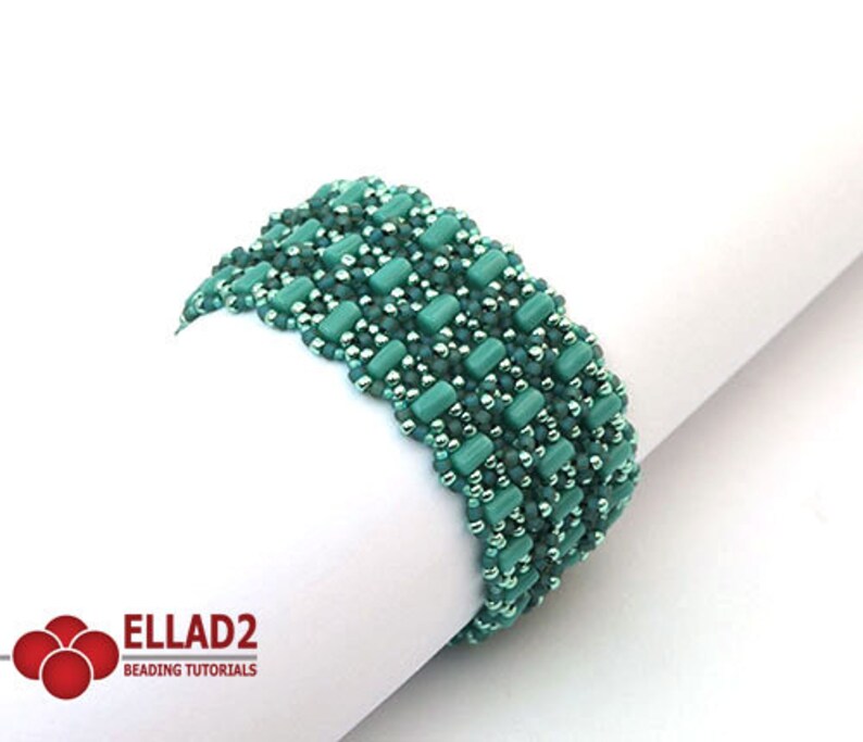 Op de afbeelding: Een groene kralen armband met een geweven patroon. De armband is gemaakt met kleine, ronde kralen en grotere, rechthoekige kralen.