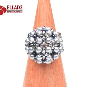 May include: A silver beaded ring with a round, spherical design. The ring is displayed on a wooden ring stand.