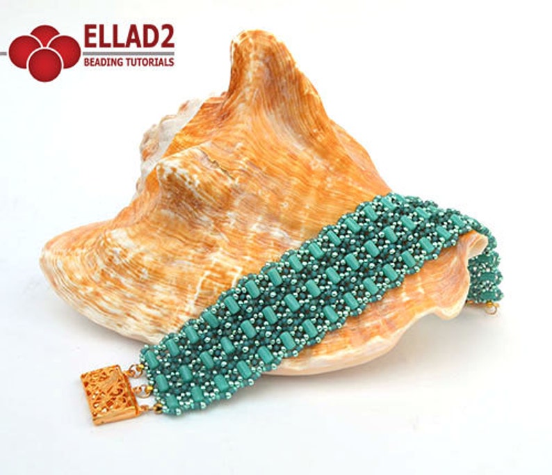 Op de afbeelding: Een tealblauwe kralen armband met een gouden sluiting, liggend op een schelp. De armband is gemaakt met kleine, vierkante kralen en heeft een geweven patroon. ELLAD2 Beading Tutorials.