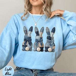 May include: Pale blue sweatshirt with three rabbit appliqués made from denim and patterned fabrics. Each rabbit has a bow and a fluffy tail. The words "Light Blue" are visible on the bottom left of the image.