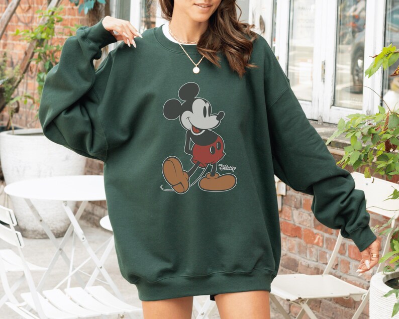 May include: A dark green sweatshirt with a Mickey Mouse graphic. The cartoon character is in black, red, and brown, with the Disney logo beneath. The sweatshirt has long sleeves and a crew neck.