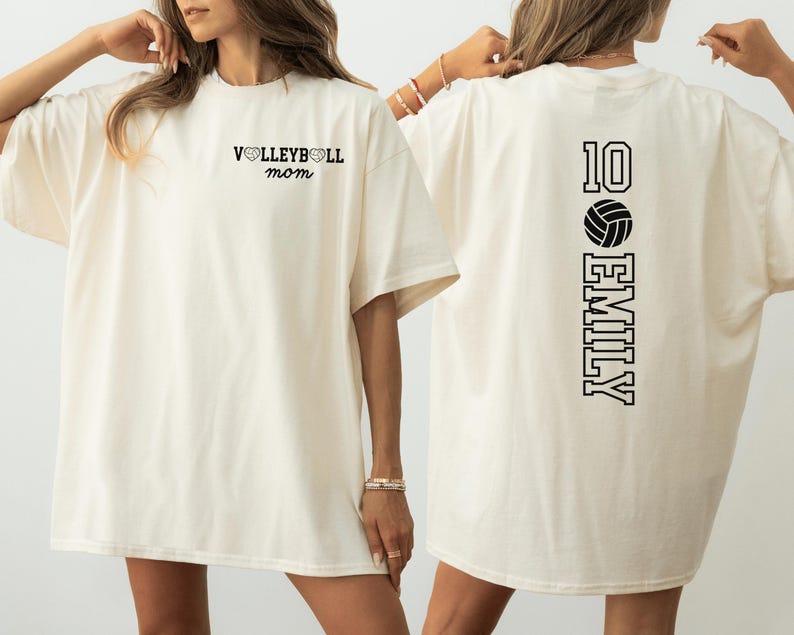 May include: Cream-colored t-shirt with black text. The front reads "VOLLEYBALL mom" above the chest. The back features the number "10", a volleyball graphic, and the name "EMILY" in a vertical layout.