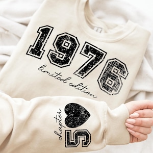 May include: Cream-colored sweatshirt with the year "1976" in a distressed black font, with "limited edition" below. The sleeve features a black heart and the text "chapter 5".