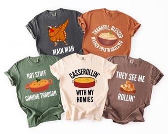 May include: Five t-shirts in various colors, each with a unique graphic and text. The shirts feature phrases like "Main Man," "Thankful, Blessed, Mashed Potato Obsessed," "Hot Stuff Coming Through," "Casserollin' With My Homies," and "They See Me Rollin'."