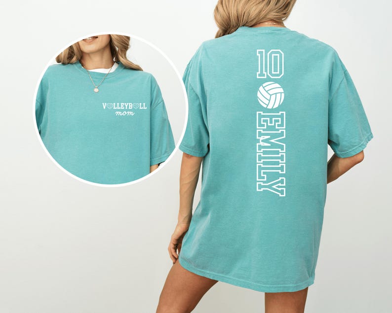 May include: A teal-colored t-shirt with the text "VOLLEYBALL mom" on the front. The back of the shirt features the number 10, a volleyball graphic, and the name "EMILY" in white lettering. The shirt has short sleeves.