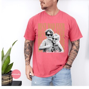May include: A red t-shirt with the text "BEST DAD EVER" in gold lettering. The shirt features a black and white photo of two children wearing sunglasses. The names "Sam & Olivia" are printed below the photo.
