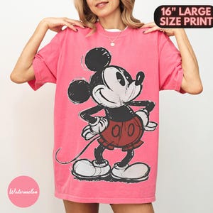 Puede incluir: Una camiseta rosa con un gran gr&aacute;fico de Mickey Mouse. El personaje de dibujos animados es en blanco, negro y rojo. La camiseta tiene el texto "16" LARGE SIZE PRINT" en la parte superior y "Watermelon" en un c&iacute;rculo rosa en la parte inferior.