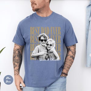 May include: Blue jean colored t-shirt with the text "BEST DAD EVER" in gold lettering. A black and white photo of two children wearing sunglasses is centered on the shirt, with the names "Sam & Olivia" printed below.