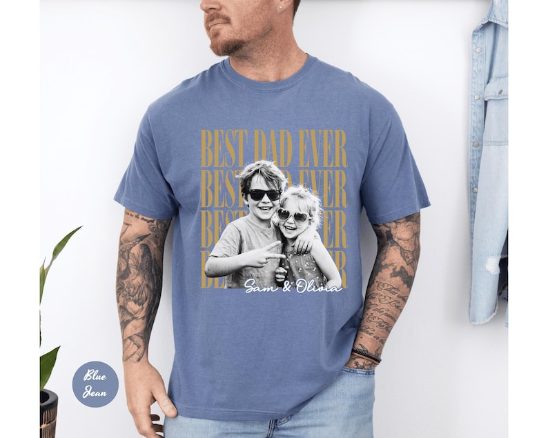 May include: Blue jean colored t-shirt with the text "BEST DAD EVER" in gold lettering. A black and white photo of two children wearing sunglasses is centered on the shirt, with the names "Sam & Olivia" printed below.