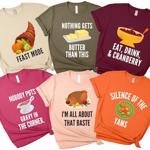 May include: A collection of six colorful t-shirts with Thanksgiving-themed graphics and text. Designs include a cornucopia, butter, a bowl of cranberries, a roasted turkey, gravy, and yams. Each shirt has a different color.