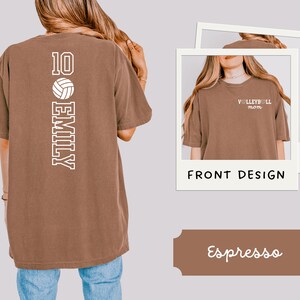 May include: Espresso-colored t-shirt with a volleyball design. The back of the shirt features the number 10, a volleyball graphic, and the name "EMILY" in a vertical layout. The front design shows "VOLLEYBALL mom" in white.
