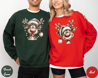 Op de afbeelding: Bosse groene en rode sweatshirts met een cartoon rendier ontwerp. Het rendier heeft een blauwe hoed, een rode neus en is versierd met lichtjes. De sweatshirts zijn een feestelijke keuze voor de feestdagen.